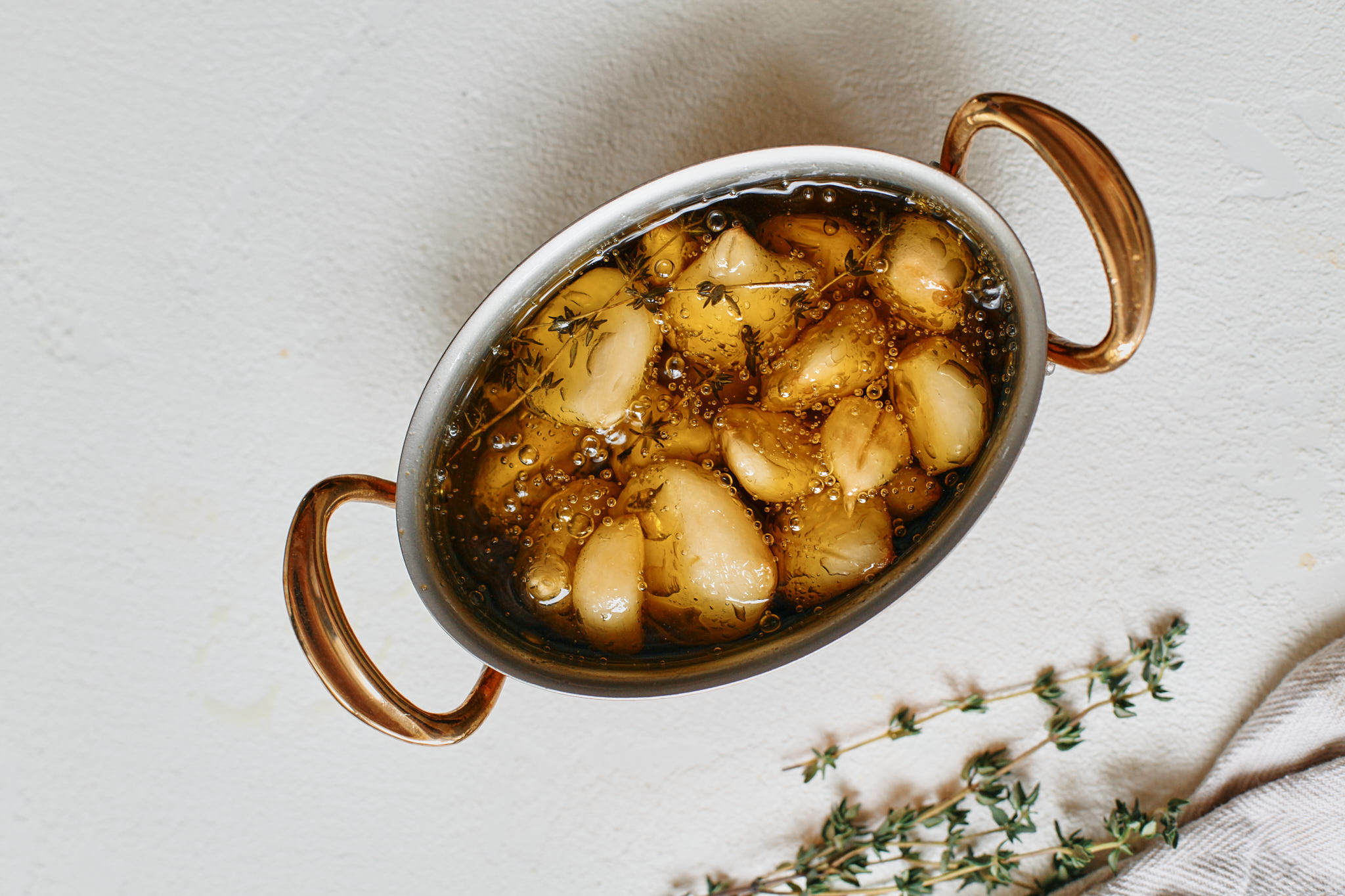 garlic cloves submerged in olive oil with fresh thyme - after being slow cooked
