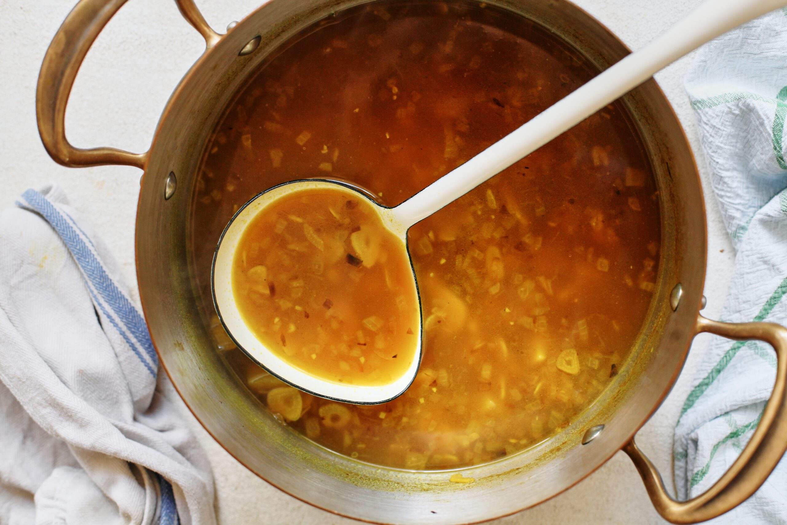 golden garlic soup in a large pot with a ladle