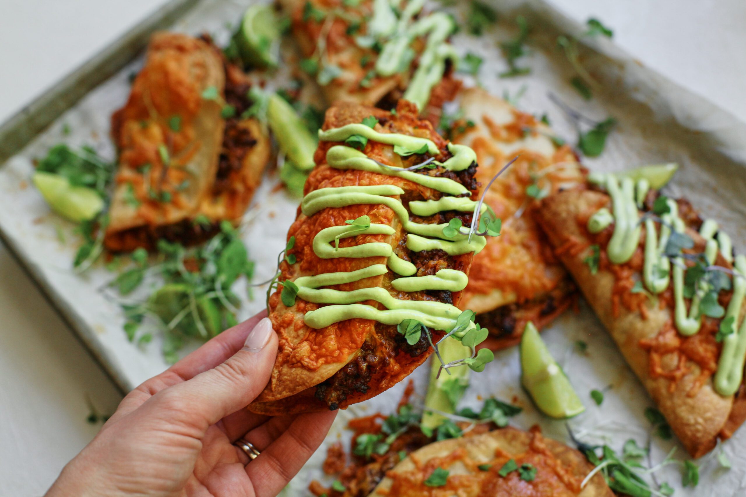 a hand holding a sheet pan beef taco dressed with avocado lime crema and cilantro