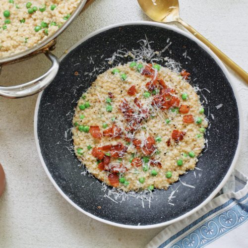 cheesy bacon pastina with peas, served in a black bowl