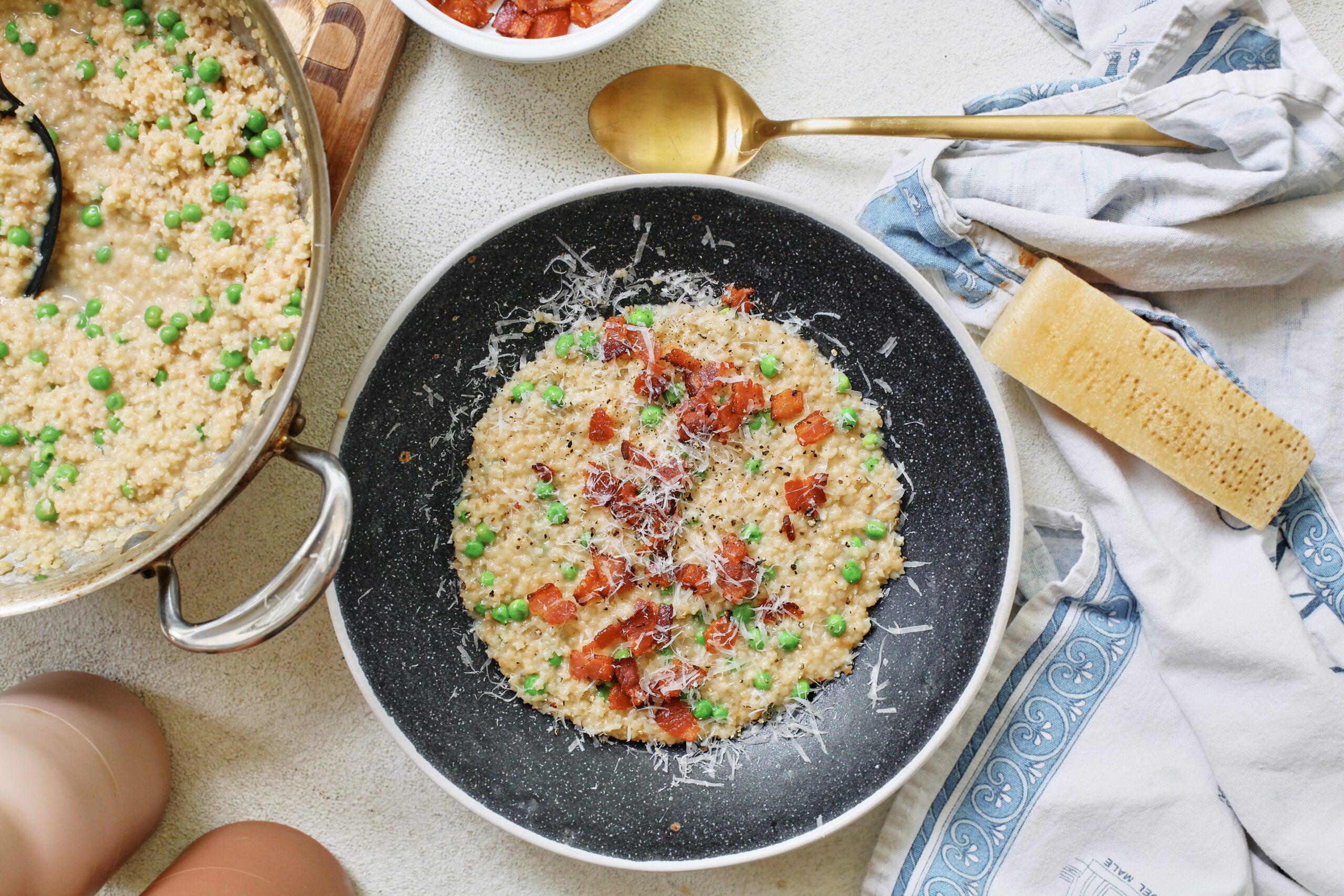 cheesy bacon pastina with peas, served in a black bowl. The full pan of the dish is to the left of the plated portion