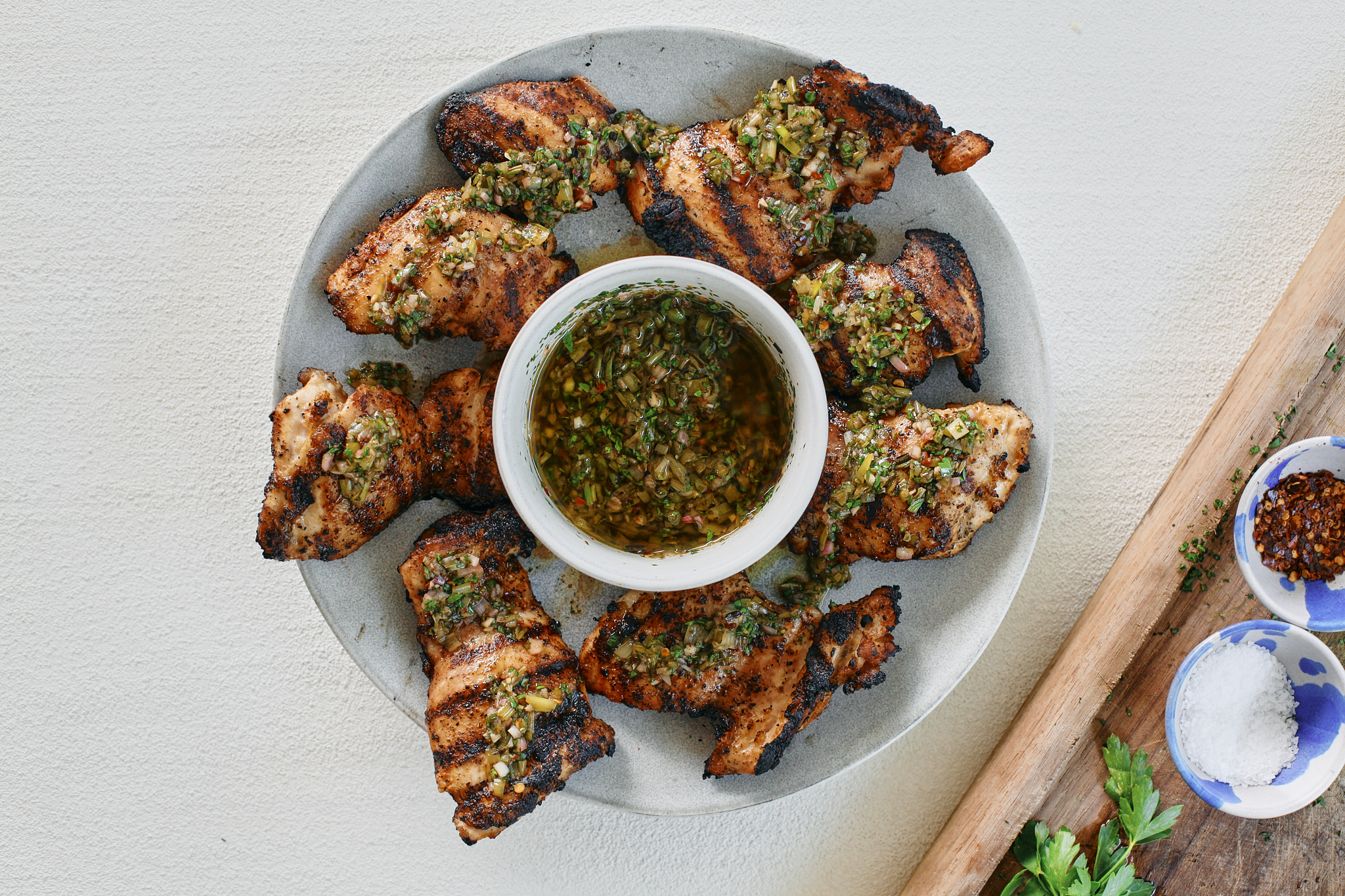 grilled chicken thighs with a bowl of chimichurri sauce