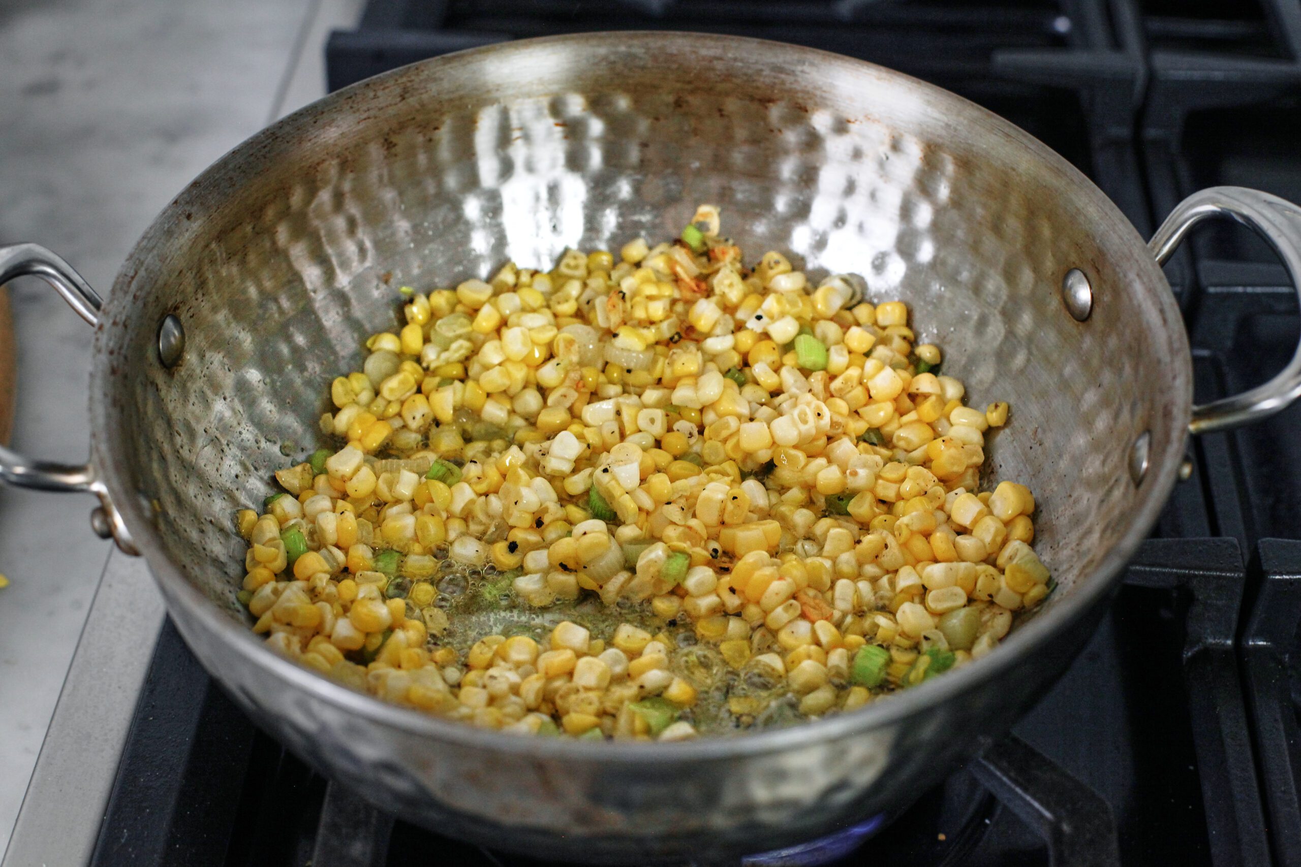 corn, green onions, and garlic sauteeing in a pan