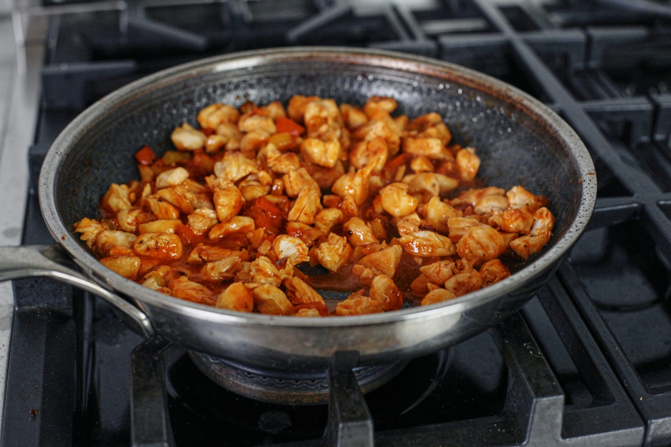 cooked chicken and bell pepper mixture in a pan on the stove, with buffalo sauce added