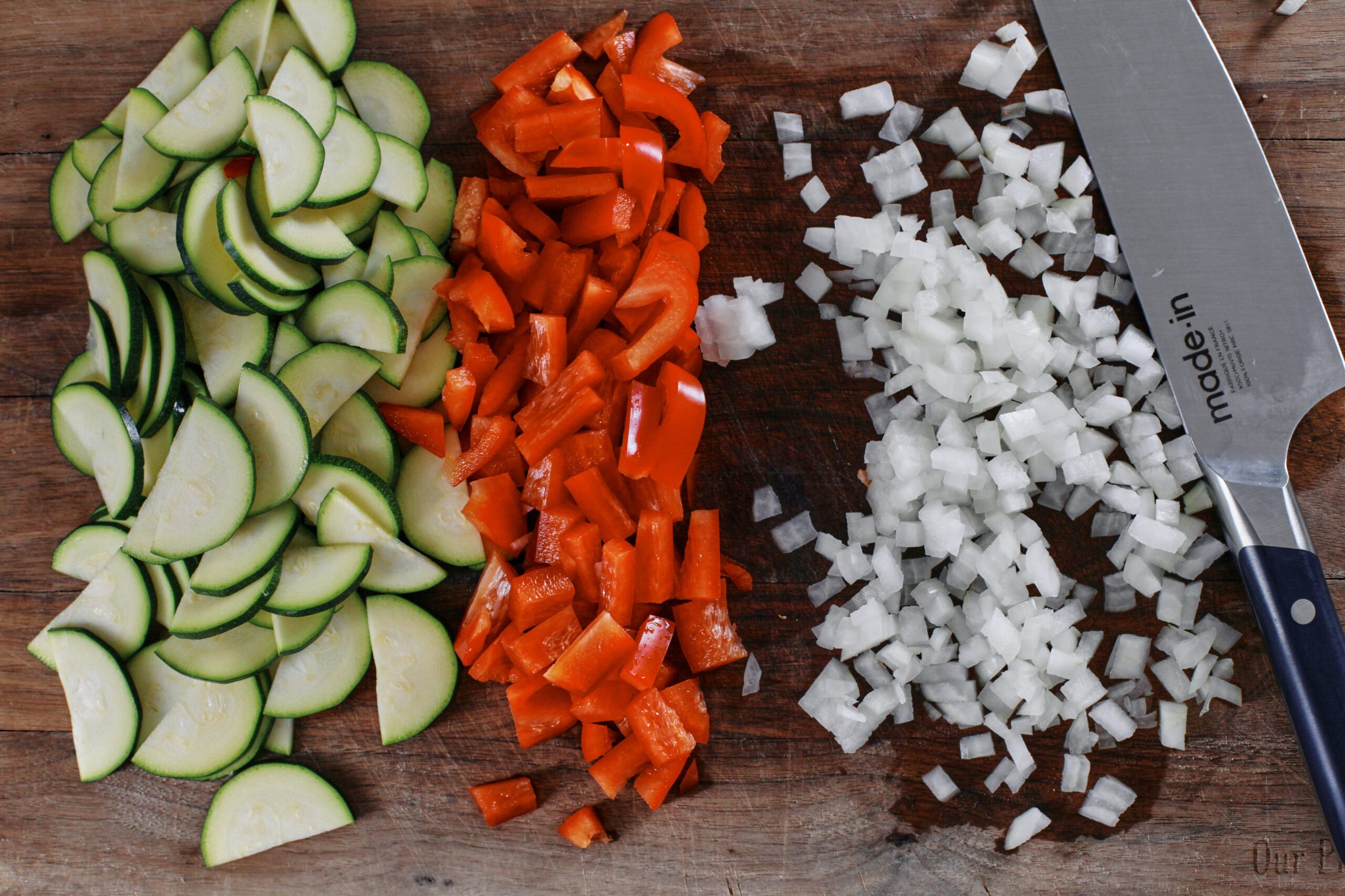 chopped zucchini, red bell pepper, and onion on a wooden cutting board