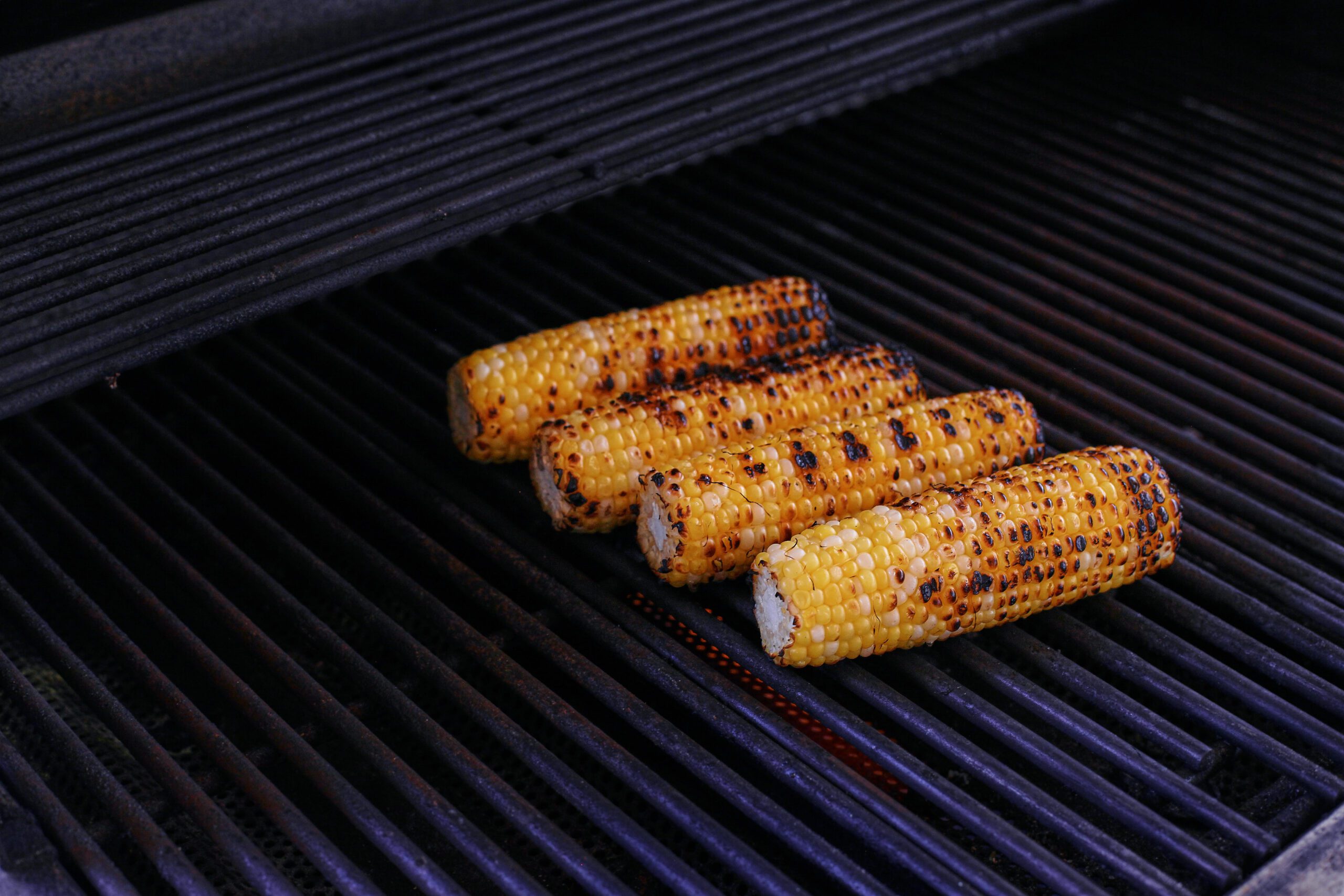 four cobs of corn cooking on the grill