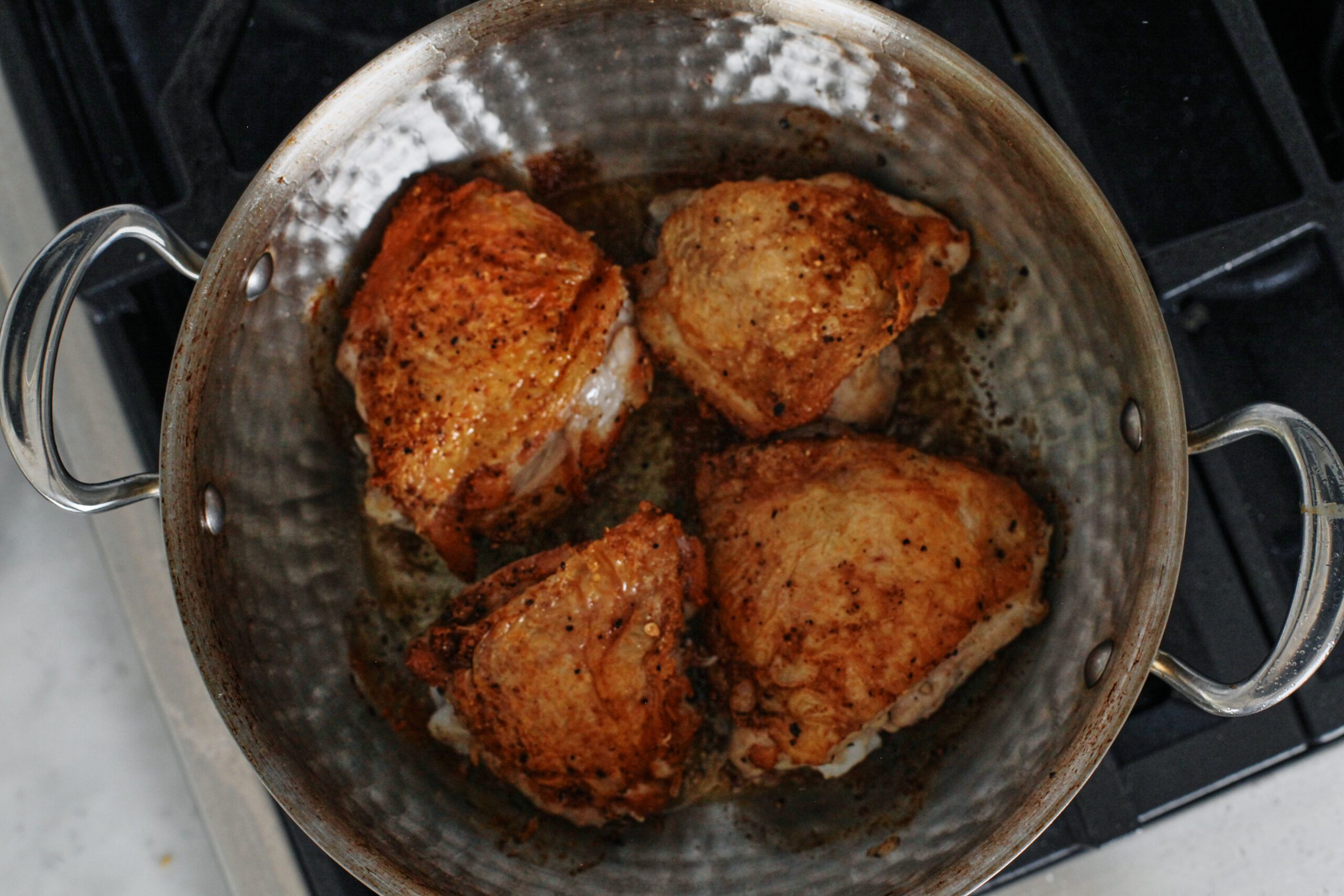 chicken thighs cooking in a hammered stainless steel pan on the stove