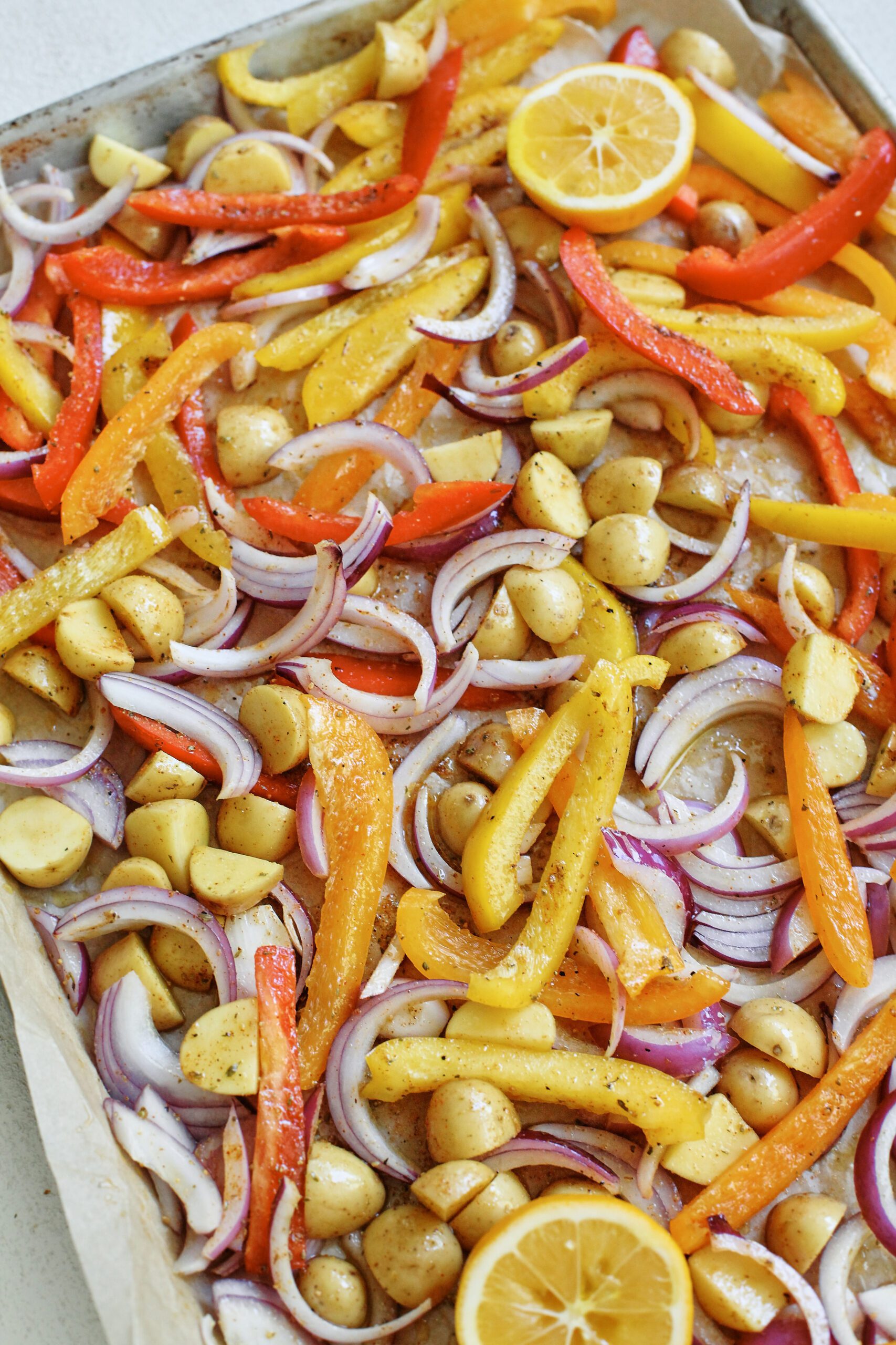 Sheet Pan Sausage, Peppers & Potatoes 4 peppers, potatoes, and onions on a sheet pan ready to roast in the oven