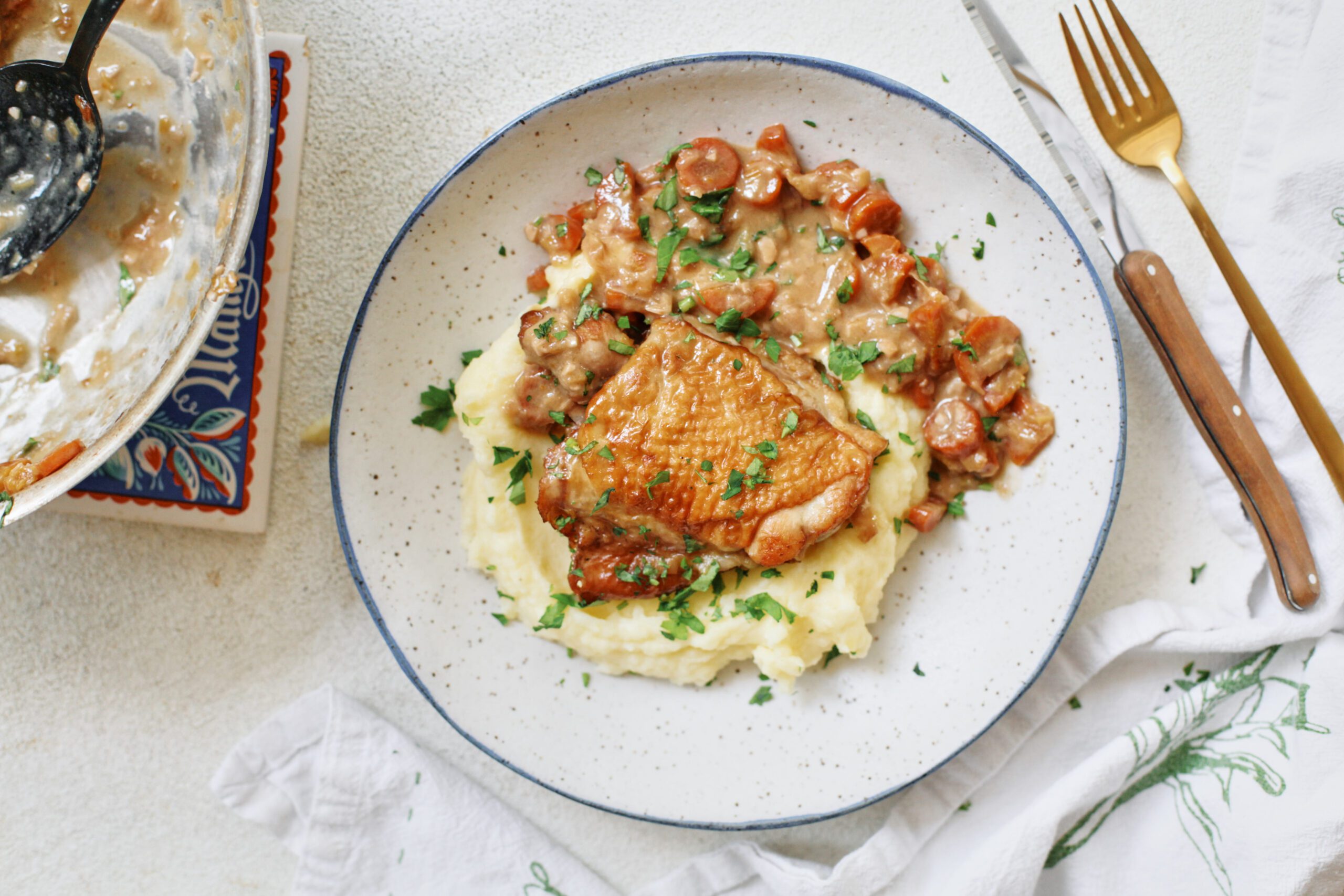 plated coq au vin blanc over a bed of creamy mashed potatoes with fresh Italian parsley on top