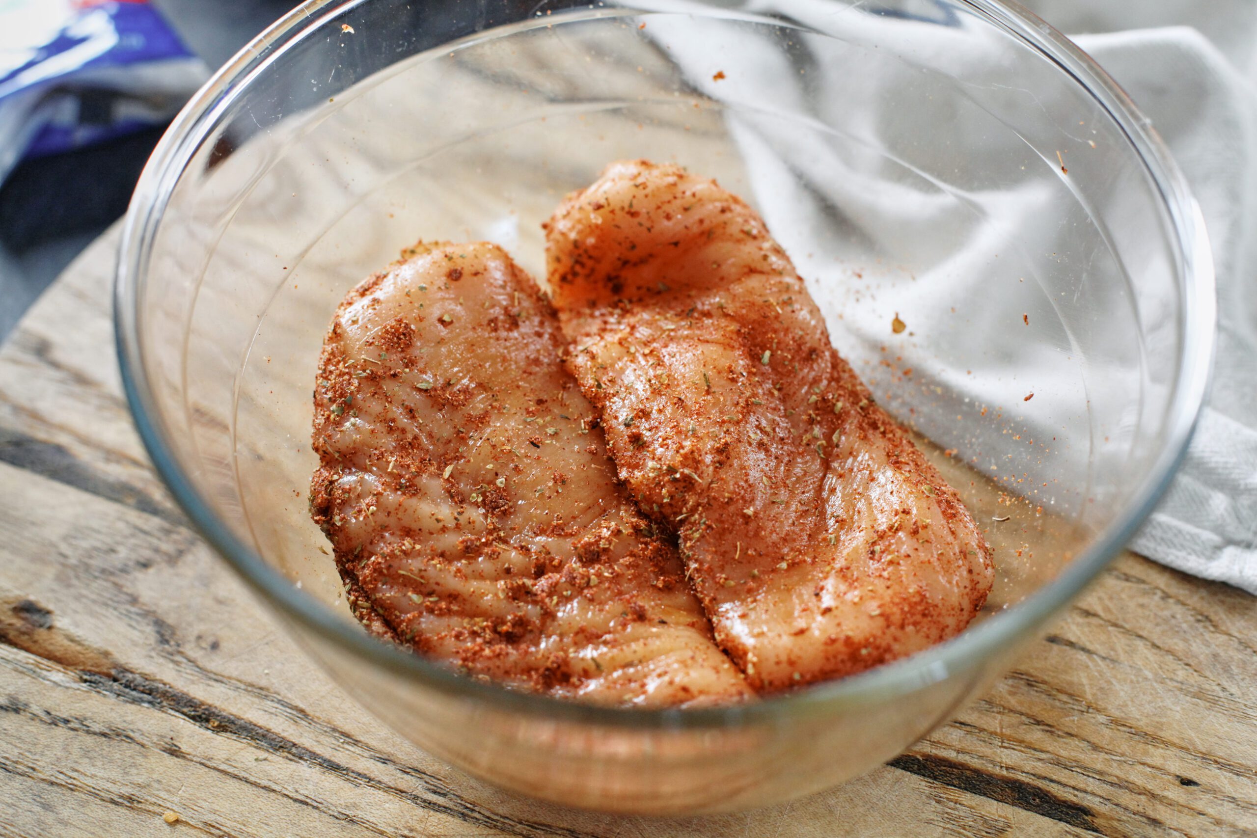 two chicken breasts marinating in a large glass bowl
