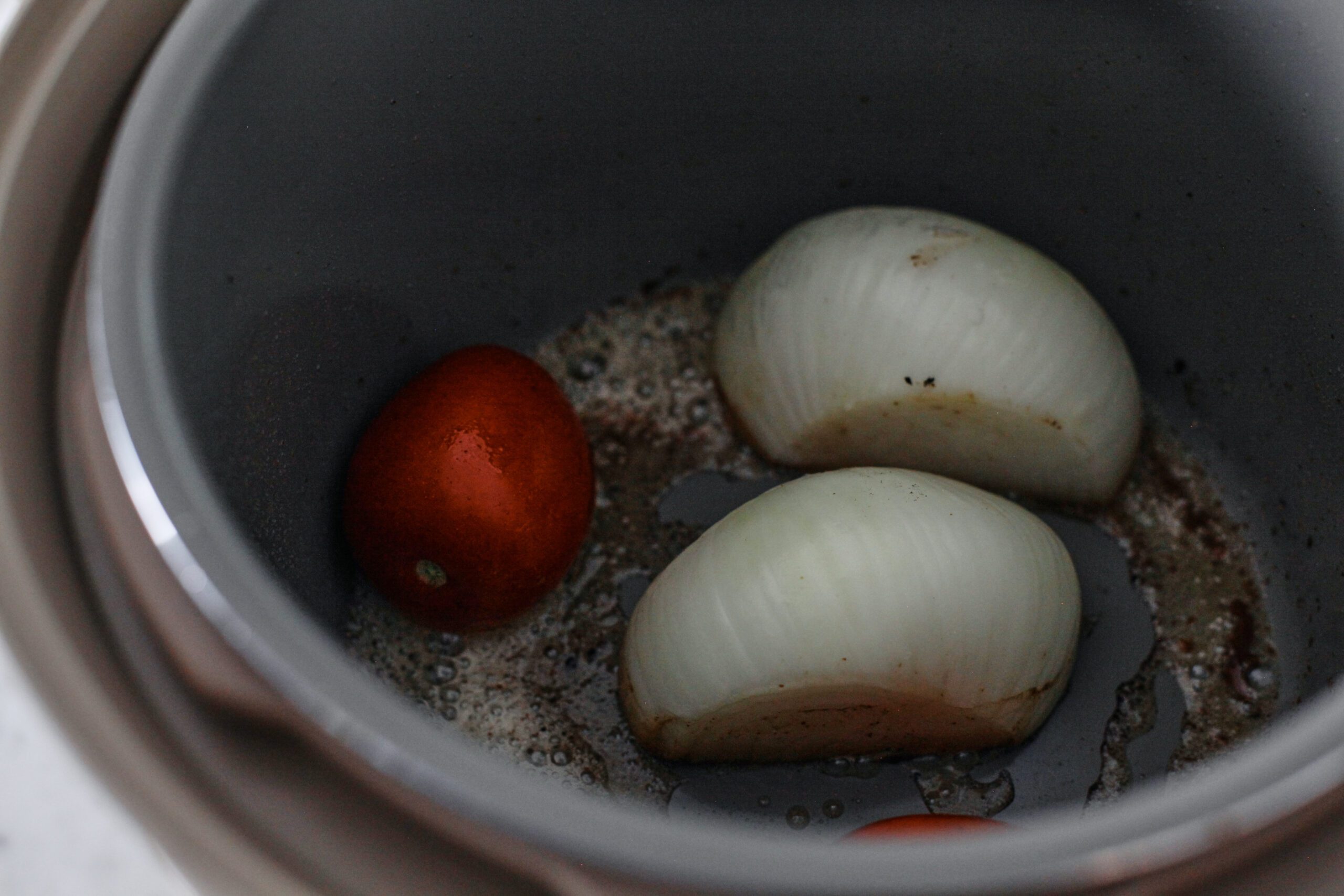a roma tomato and a halved white onion being seared in the pressure cooker