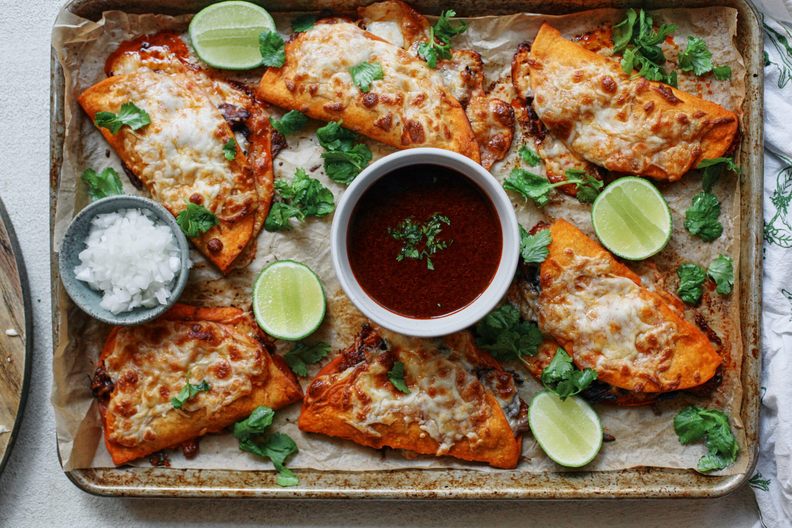 birria sheet pan tacos + a bowl of consomme dressed with cilantro, lime wedges, and a bowl of chopped white onions