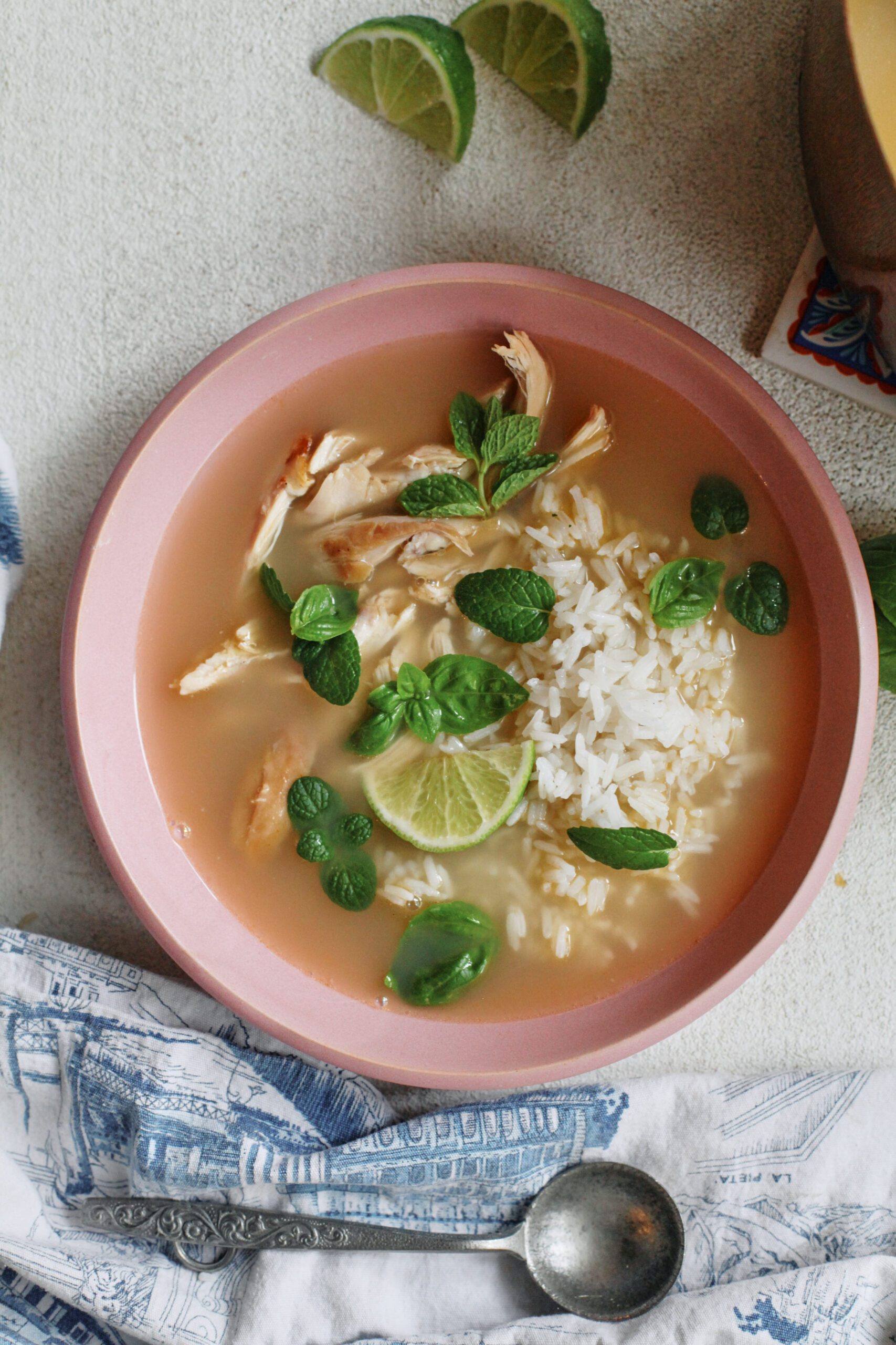 Overhead photo of a bowl of ginger chicken rice soup with shredded rotisserie chicken, fluffy white rice, and fresh mint and basil on top, garnished with a lime wedge