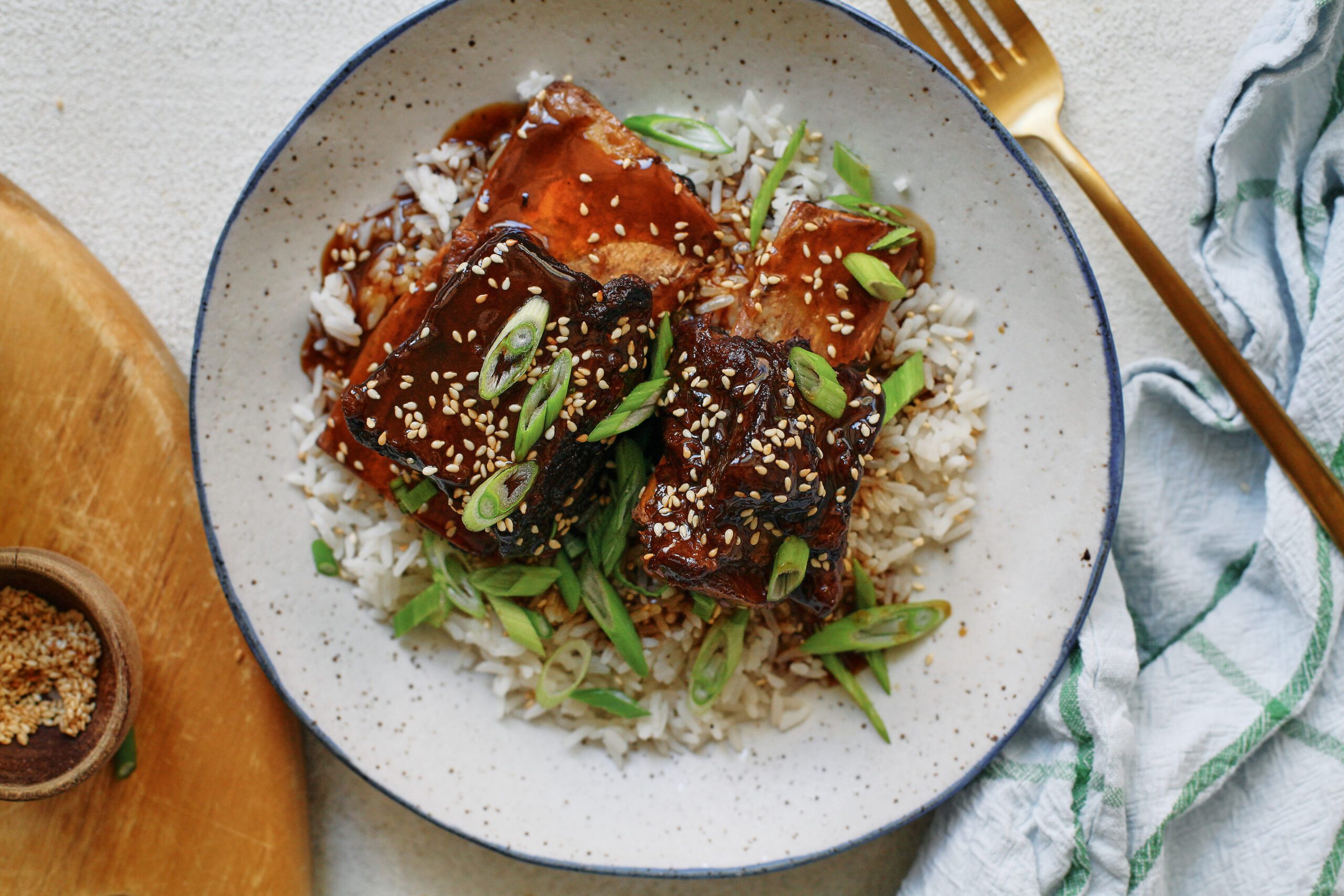sticky soy and citrus short ribs over white rice, garnished with green onions and sesame seeds